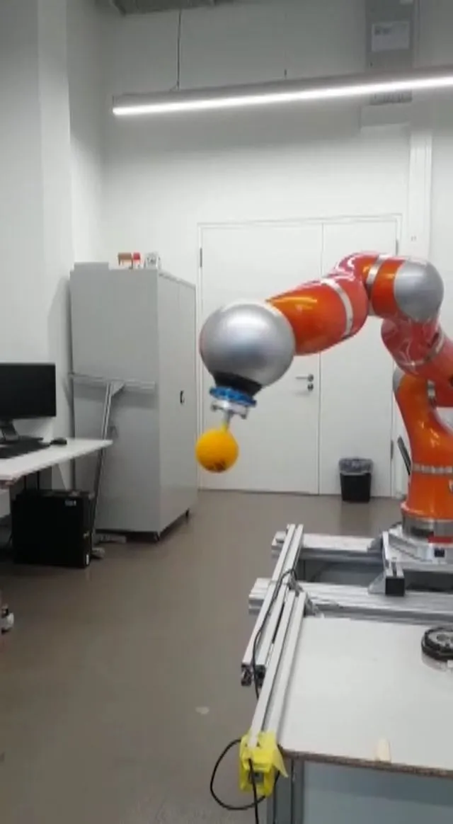 Orange industrial robot arm holding a ball in a lab