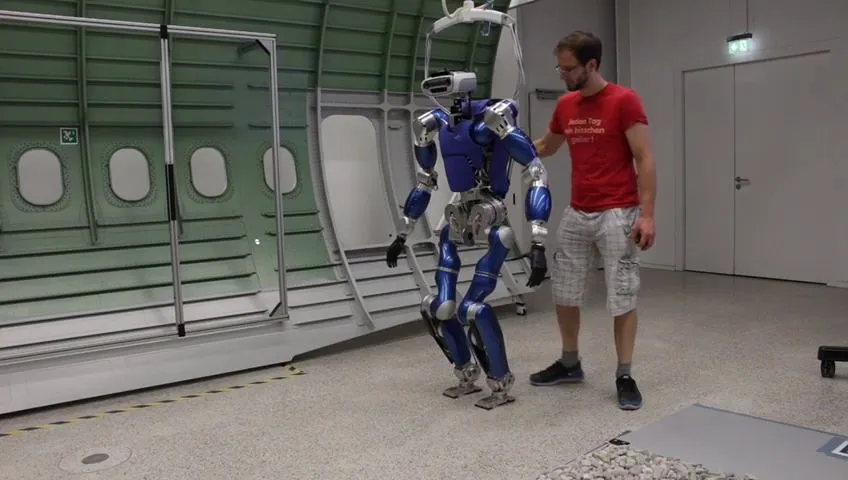 Engineer guiding a torque-sensorized humanoid robot by hand in a test hall